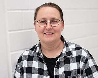 Porträt einer Person in einem karierten Hemd vor einer weißen Wand.